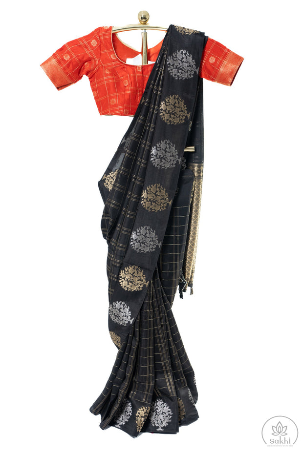 Black saree with gold patterns draped over a red blouse on a white background